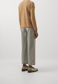 Beige gestrickter Pullover mit strukturiertem Muster; graue weite Jeans; schwarze Schuhe mit Absatz im Schlangenprint.