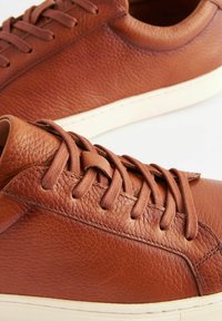 Bruna lädersneakers med en texturerad yta, rund tå, platta snörningar och en krämfärgad gummisula. Minimalistisk design med subtila sömmar.