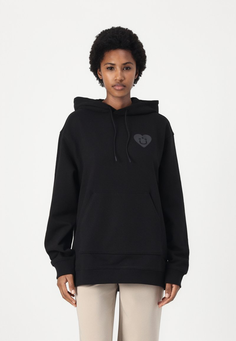 Black hooded sweatshirt in soft fabric, featuring a front pocket and a heart-shaped logo with a smiley face. Relaxed fit, long sleeves.