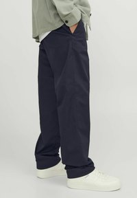 Mørkeblå bredbenede bukser lavet af bomuldsblanding, med sidelommer og en glat tekstur, parret med hvide sneakers.