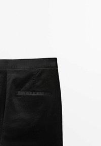 Pantalon en velours côtelé noir centré sur la ceinture élastique et une unique poche passepoilée à l'arrière, sur un fond blanc uni.