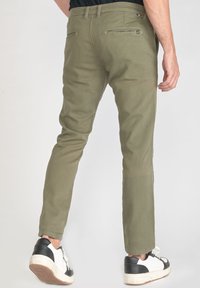 Chino en coton vert olive avec une coupe fuselée, poches avant et arrière, et zip. Associé à des baskets noir et blanc.