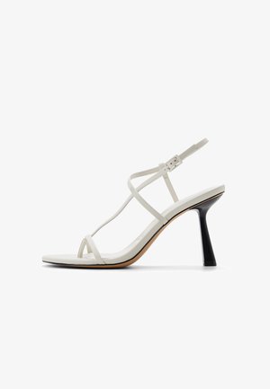 Sandale blanche à talon haut avec lanières, talon noir effilé et boucle de cheville réglable, vue de profil sur fond blanc.