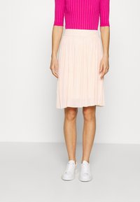 Gonna a pieghe rosa chiaro con una cintura liscia, abbinata a una maglietta a coste rosa brillante e sneakers bianche.