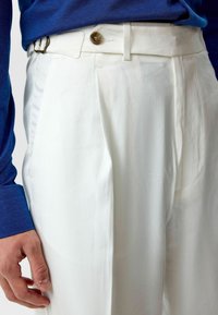 Witte geplooide broeken met een gladde textuur. Voorzien van een knoopsluiting en een rechte voorkant. Gecombineerd met een blauwe langemouwen overhemd.
