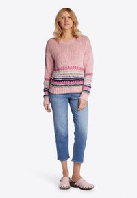 Rosa gestrickter Pullover mit mehrfarbigen horizontalen Streifen, Rundhalsausschnitt und gerippten Bündchen, kombiniert mit hellblauen, cropped Jeans und rosa Clogs.