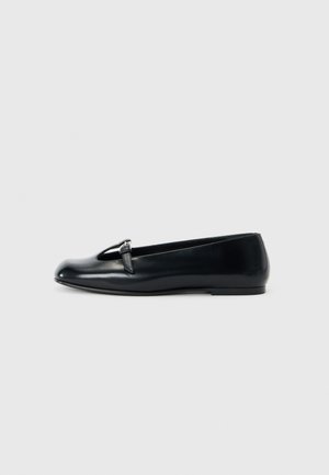 Ballerines en cuir noir avec une pointe ronde, présentant un design découpé et un petit accent de boucle en argent. Semelle plate pour plus de confort.