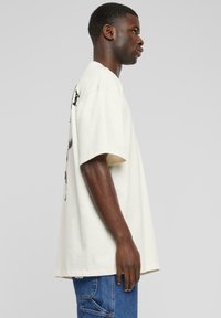 Överdimensionerad vit bomull t-shirt med rund halsringning. Har korta ärmar och ett grafiskt tryck på baksidan. Bärs med blå denimjeans.