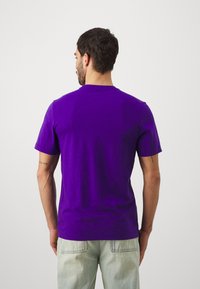 T-shirt court à manches courtes en coton doux de couleur violette. Présente une coupe régulière et une texture lisse. La vue arrière montre un design simple sans motifs.