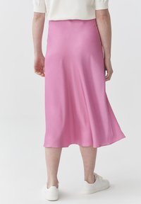 Larga falda rosa hecha de tela suave y fluida. Presenta un dobladillo acampanado y se combina con zapatillas blancas.