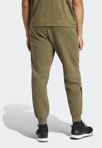 Calças de jogging verde-azeitona feitas de tecido texturado, com pernas ajustadas e um cós elástico, combinadas com sapatilhas de desporto pretas.