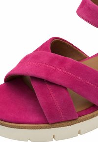 Sandali in suede fucsia con cinturini incrociati, una soletta marrone chiaro e una suola piatta bianca con un bordo texturizzato.