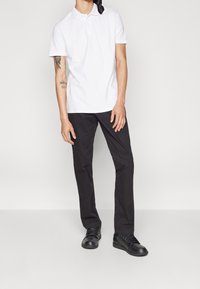 Bílá polokošile s límečkem, černé slim-fit kalhoty a černé tenisky. Má jednoduchý design a přiléhavý st řih.