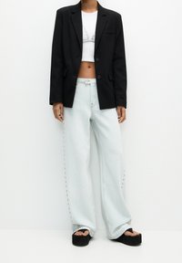 Blazer noir, haut blanc court, jean large bleu clair avec détail de couture latérale, et sandales compensées noires.