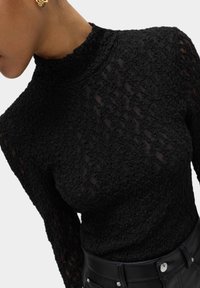 Sort blonderede turtleneck top med tekstureret mønster, lange ærmer og høj halsudskæring, parret med en sort, tætsiddende talje med hardware detaljer.