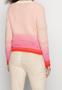 Sweter dzianinowy z gradientowym wzorem od jasnego różu do intensywnej koralowej barwy, z teksturowanym wykończeniem i krótkim krojem. W zestawie z puszystymi kremowymi spodniami.