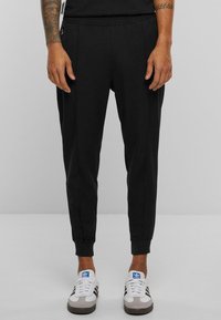Crne jogging hlače od mekog materijala, sa slim fit krojem, elastičnom ušitkom, bočnim džepovima i uskim manžetama. Nosivo uz casual tenisice.