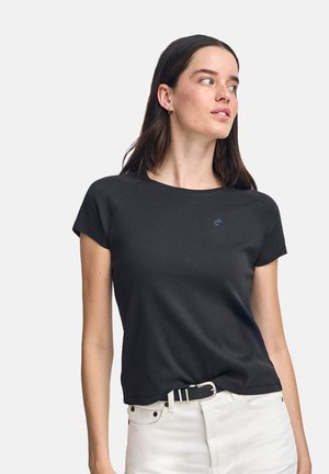 Schwarzes T-Shirt mit kurzen Ärmeln aus weichem Stoff, Rundhalsausschnitt und kleinem blauen Logo auf der Brust, kombiniert mit weißen Jeans und einem Gürtel.