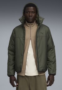 Jachetă puf în nylon verde închis, cu glugă, asociată cu un top crem cu fermoar. Prezintă manșete ribbate și un mic logo negru pe piept.