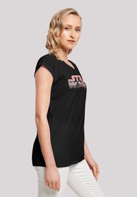 Melnas kokvilnas T-krekls ar rozā "STAR WARS" grafiku, ar brīvu piegriezumu un īsām piedurknēm, izvietots uz neitrāla fona.