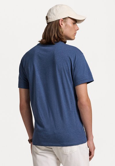 Blå kortärmad t-shirt visad från baksidan, tillverkad av mjukt tyg med en slät textur. Matchad med en ljusfärgad keps.