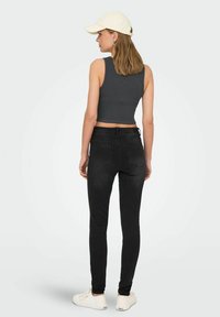 Szara krótka koszulka na ramiączkach i czarne skinny jeansy z wysokim stanem i tylnymi kieszeniami, zestawione z białymi sneakersami i beżową czapką.
