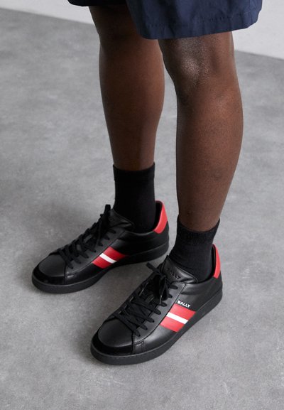 Sneakers in pelle nera con strisce rosse e bianche, punta tonda, lacci neri e una finitura texturizzata. Accentati da un logo sul lato.