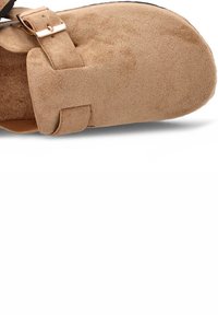 Zapatilla de ante marrón con puntera redondeada, correa ajustable con herrajes dorados y una textura suave. Suela de goma negra visible en la parte inferior.