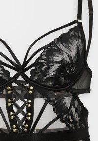 Black lace lingerie top with floral patterns, thin straps, and crisscross ribbon detailing with gold eyelets at the front center.