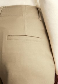 Beige corduroy broek met een gladde textuur, voorzien van een enkele achterzak en subtiele stikdetails. Ontworpen voor een aangesloten look.