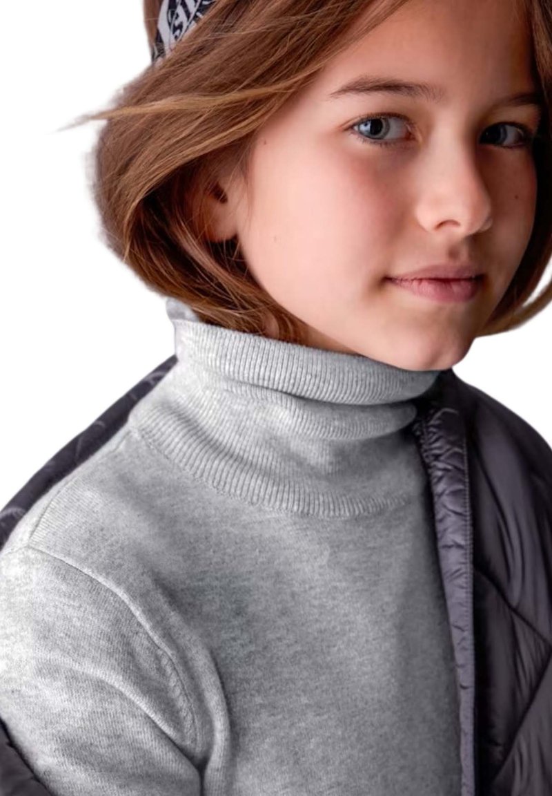 Maglione a collo alto grigio chiaro con collo a costine, indossato sotto un giubbotto imbottito grigio scuro, realizzato in un tessuto morbido e testurizzato.