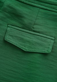 Close-up van groene stof met een klepzak met nette stiksels en een soepele textuur, waarbij de vorm en kleurdetails worden benadrukt.
