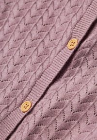 Gaiši purpursarkans adīts kardigans ar teksturētu zigzag rakstu, ar taisnu apkakles līniju un divām koka pogām priekšpusē.