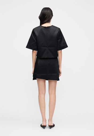 Melns īss tops ar īsām piedurknēm, kopā ar melnu mini svārku. Audums ir gluds un patīkams pieskārienam. Plāns siluets, aizmugurē rāvējslēdzēja detaļa.