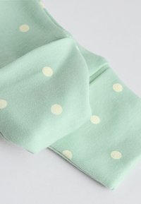 Világoszöld szövet fehér pöttyökkel, összehajtva, a kötött textúra jól látható, egyszínű világosszürke háttéren.