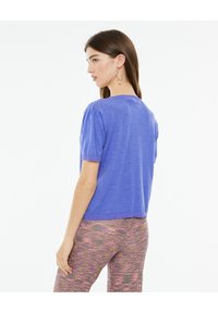 Lightweight, short-sleeve pullover in vibrant purple with ribbed trim and gathered shoulders. Paired with multicolored textured pants.