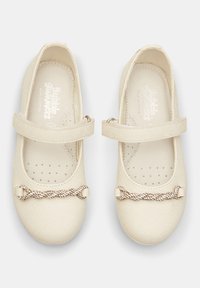 Weiße synthetische Leder-Mary-Jane-Schuhe mit runder Zehenpartie, Knöchelschnalle und einem dekorativen Kettendetail an der Vorderseite. Flache Sohle, durchlässiges Innenfutter.