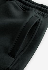 Pantalones deportivos negros con cintura elástica, que cuentan con un bolsillo lateral y una textura de tela suave. Diseño minimalista, vista en primer plano.