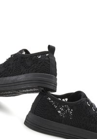 Black lace sneakers featuring a textured knit upper, rubber sole, and flat lace closure, with a pull tab at the heel for easy wear.