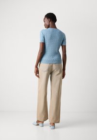 Maglione corto azzurro a maniche corte con un design a treccia testurizzato, abbinato a pantaloni beige a gamba larga e mules azzurri con tacco a blocco.