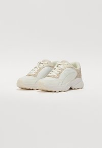 Adidași albi cu un accent texturat de culoare bej, guler căptușit și șireturi. Prezintă o talpă căptușită și un logo pe lateral.