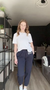 White cotton t-shirt paired with navy drawstring sweatpants featuring "GAP" logo. Model wears white sneakers, showcasing casual loungewear.
