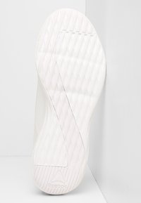 Witte sportieve schoenzool met een gestructureerd oppervlak, diagonale groeves en een driehoekig logo op de hiel.