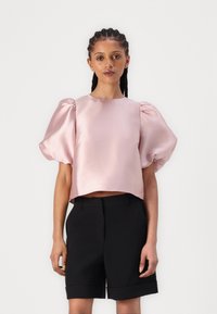 Rosa sateng kort topp med pufferm som er parert med svarte skreddersydde shorts med oppbrettede kanter. Glatt tekstur og rene linjer.