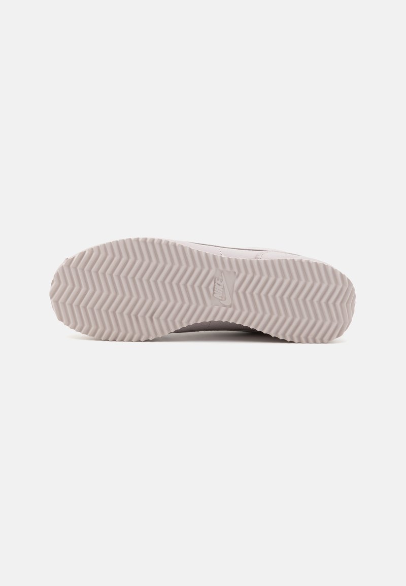 Suela de zapatilla gris claro con un patrón texturizado en zigzag para un mejor agarre, que presenta un logo sutil cerca del talón y bordes suaves.