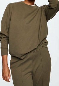 Haut à manches longues vert olive, coupe ample et encolure arrondie, assorti à un pantalon fuselé assorti, en tissu texturé.