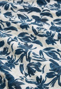 Tissu blanc avec imprimé botanique bleu présentant des feuilles et des fleurs abstraites, affiché avec des plis doux et une surface texturée.