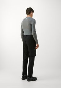 Fitted gray long-sleeve top with a contrast panel, paired with black cargo pants featuring pockets and elastic waistband, worn with black sneakers.