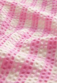 Textil s alternujícími růžovými a bílými pruhy, s texturovaným povrchem a vyvýšenými tečkami, měkkou tkaninou a hladkým povrchem.