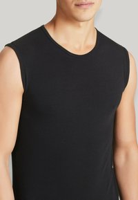 Canottiera nera in cotone senza maniche con scollo rotondo, caratterizzata da una trama liscia e da un design attillato, che mette in evidenza spalle e braccia.